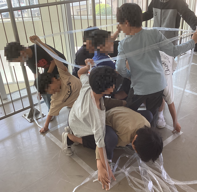 テープで作る立方体の中に入る児童たち