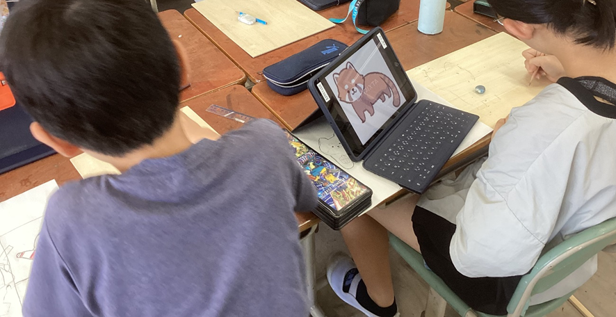 タブレットでイラストを見ながらベニヤ板に絵を描いているようす