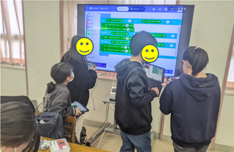 スクリーンのお手本を見ながらプログラミングする児童