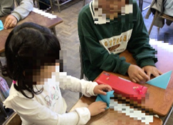 1年生の隣で折り方を教える6年生